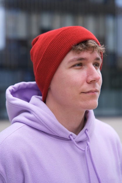 Portret van een jonge gelukkige man of tiener in hoodie en hoed die buiten naar de camera kijkt