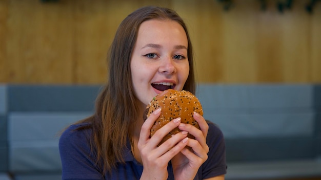 Portret van een jonge gelukkige vrouw of een mooi tienermeisje dat snel junkfood eet, een smakelijke burger en