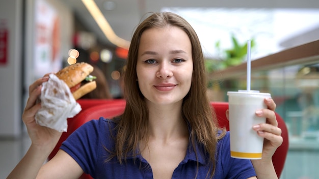 Foto portret van een jonge gelukkige vrouw of een mooi tienermeisje dat snel junkfood eet, een smakelijke burger en