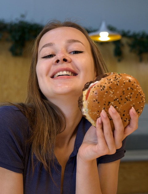 Foto portret van een jonge gelukkige vrouw of een mooi tienermeisje dat snel junkfood eet, een smakelijke burger en