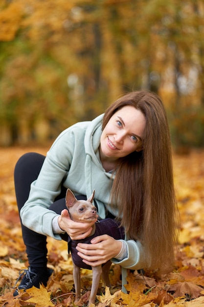 Portret van een jonge gelukkige wowan met haar hond toyterrier in haar armen in het herfstpark