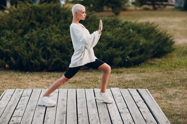 Foto portret van een jonge glimlachende duizendjarige europese kortharige vrouw die qigong taijiquan doet in het zomerpark. mooi gelukkig blond meisje buiten.