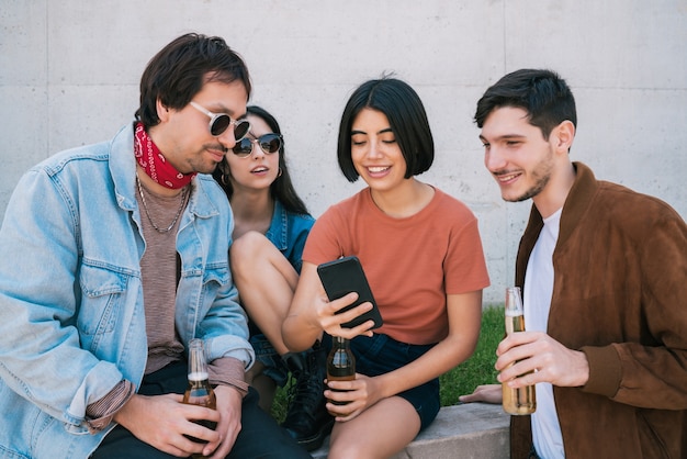 Portret van een jonge groep vrienden tijd samen doorbrengen tijdens het kijken naar iets in de smartphone buitenshuis. Technologie en vriendschapsconcept.