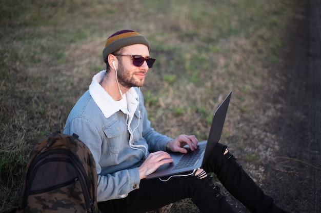Portret van een jonge hipster man met laptop buiten