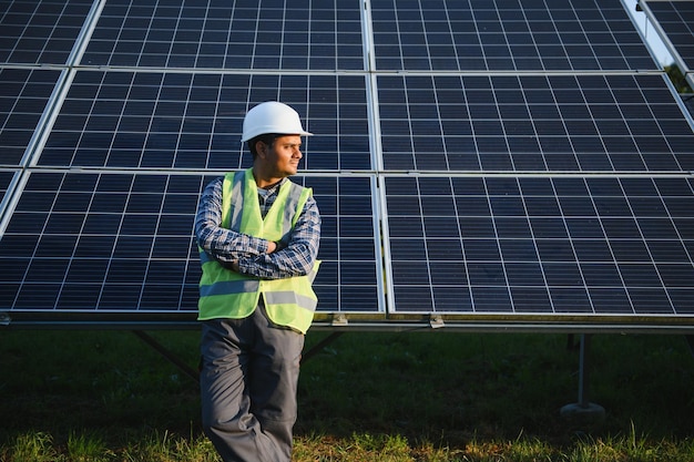 Portret van een jonge Indiase technicus met een witte harde hoed die naast zonnepanelen staat tegen een blauwe lucht Industriële werknemer installatie van een zonne-systeem