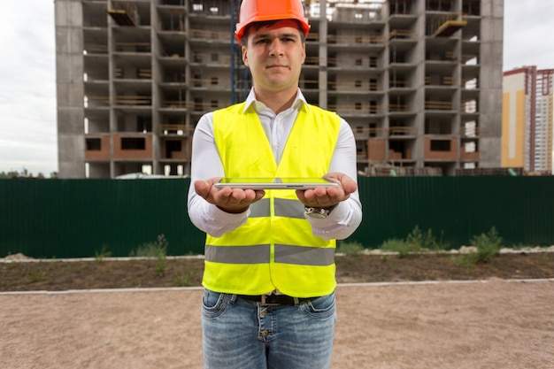 Portret van een jonge ingenieur die tegen de bouwplaats staat en een digitale tablet vasthoudt. Perfect om uw afbeelding op een tablet te plaatsen