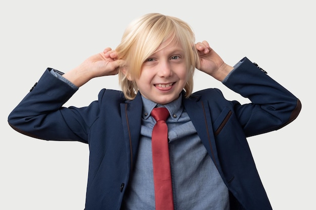 Portret van een jonge jongen met blond haar die een blauw jasje en een rode stropdas draagt en zijn oren met zijn handen vasthoudt