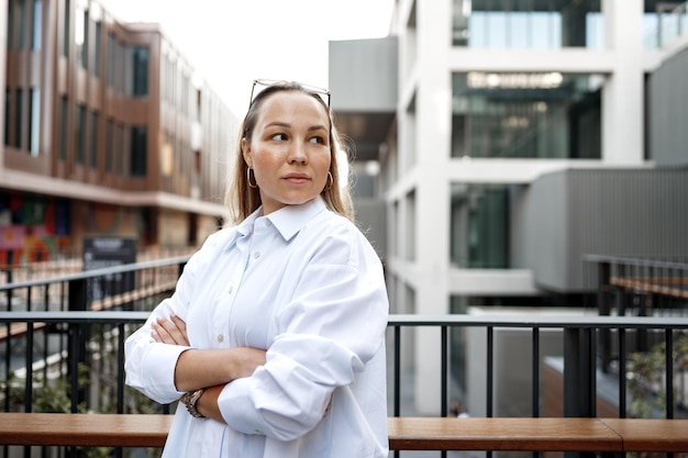 Portret van een jonge kantoorvrouw die op het balkon staat en geniet van het uitzicht op de stad