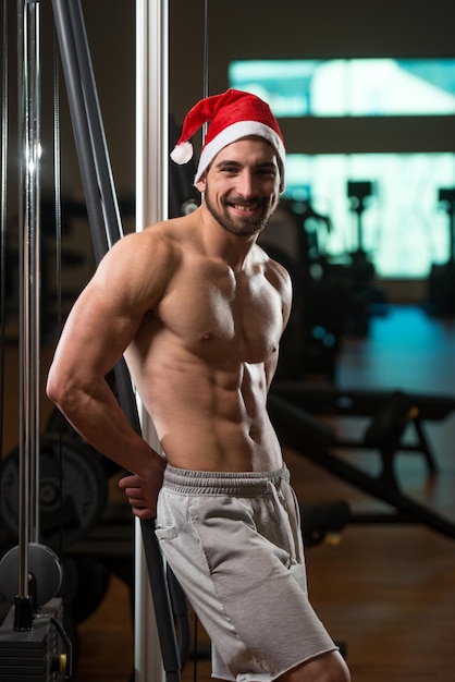 Portret van een jonge kerstman die poseert en bodybuilding laat zien in de sportschool