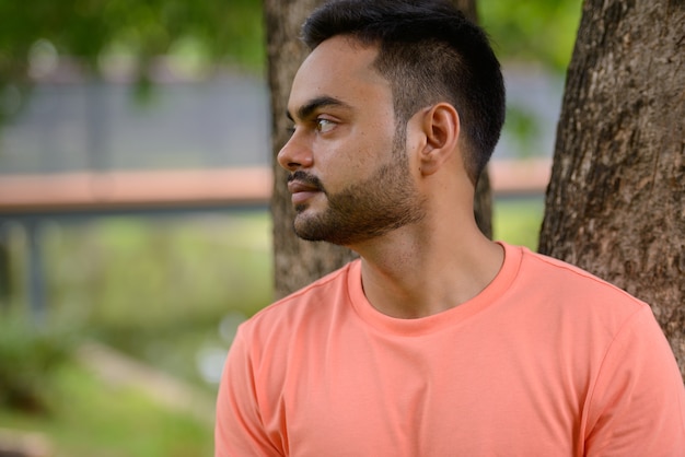 Portret van een jonge knappe bebaarde Indiase man in het park buitenshuis