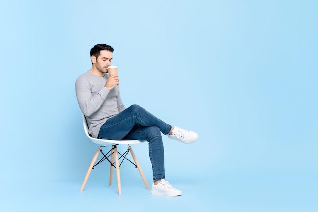 Portret van een jonge knappe blanke man die een pauze neemt terwijl hij rustig koffie drinkt in een geïsoleerde studio blauwe achtergrond