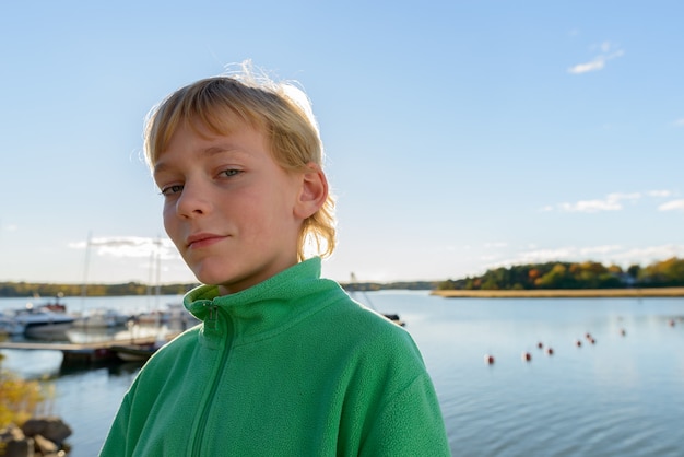 Portret van een jonge knappe jongen met blond haar op houten pier tegen uitzicht op de rivier