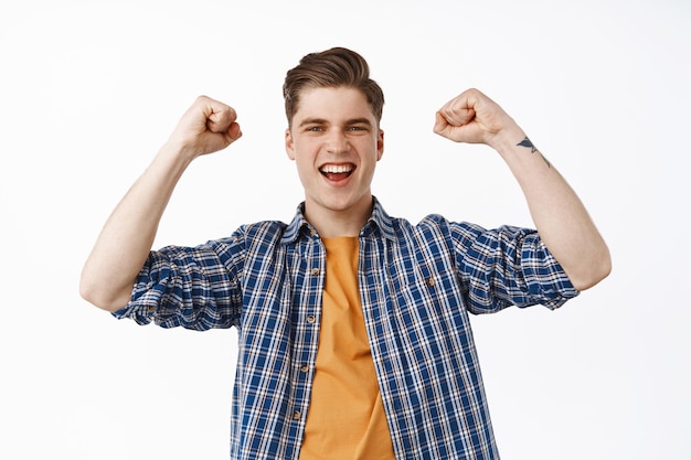 Portret van een jonge knappe man die schreeuwt van vreugde, zingen en juichen, wroeten voor team, weddenschap plaatsen, vieren, voetbalwedstrijd kijken, staande tegen een witte achtergrond.