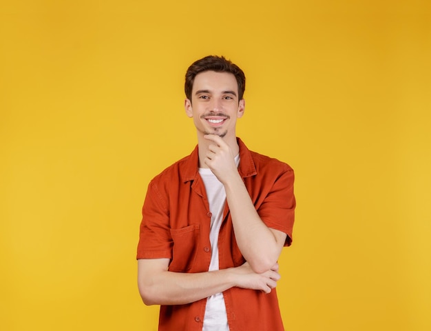 Portret van een jonge knappe man die zelfverzekerd naar de camera kijkt met een glimlach met gekruiste armen en de hand opgeheven op de kin over een geïsoleerde achtergrond