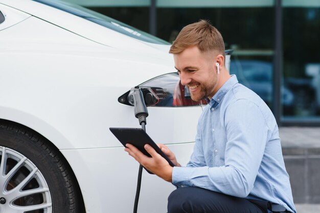 Portret van een jonge knappe man in vrijetijdskleding die staat bij het laadstation Eco elektrische auto concept