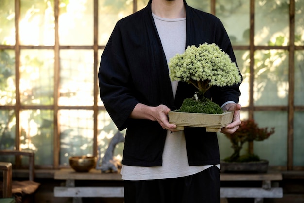 Portret van een jonge knappe man met een bonsai in zijn handen op de achtergrond van een Aziatisch theehuis