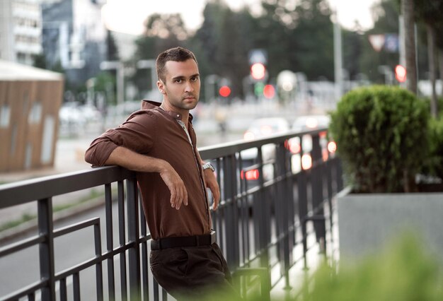 Portret van een jonge knappe man met ongeschoren haren in een bruin shirt op straat in de stad