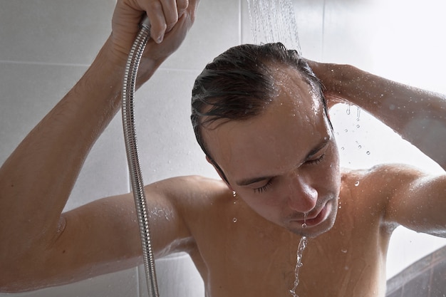 Portret van een jonge knappe man wast zichzelf met douchegel, schuimt het hoofd met shampoo in de badkamer thuis close-up