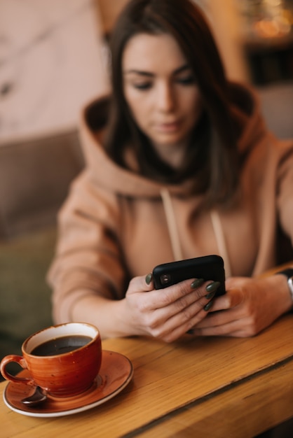 Portret van een jonge knappe vrouw die in de coffeeshop aan een houten tafel zit