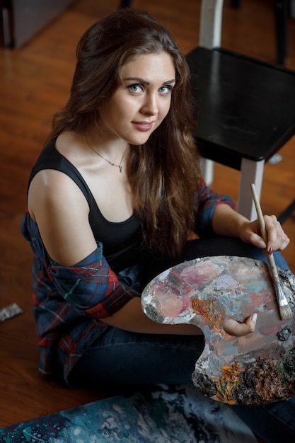 Foto portret van een jonge kunstenaar omringd door schilderijen