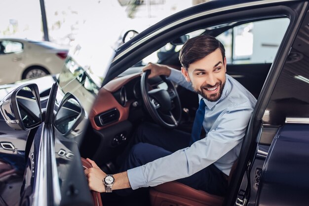 Portret van een jonge lachende zakenman die de bestuurdersdeur van de auto sluit