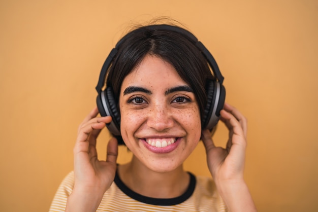 Portret van een jonge Latijns-vrouw, luisteren naar muziek met een koptelefoon tegen geel.