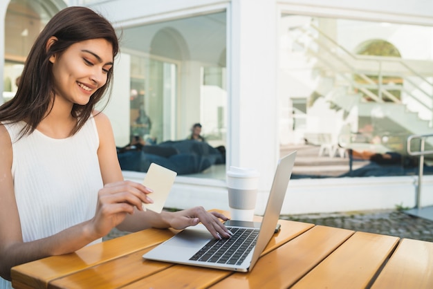 Portret van een jonge Latijns-vrouw met creditcard en laptop gebruikt om online te winkelen bij een coffeeshop. Online winkelen en lifestyle-concept.