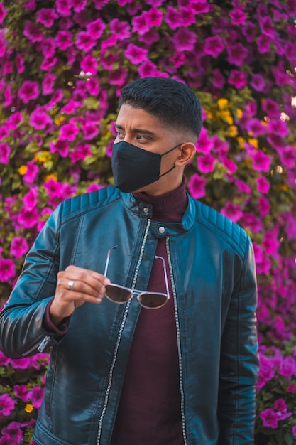 Portret van een jonge Latino met roze bloemen op de achtergrond. Jeans, leren jas en bruine schoenen