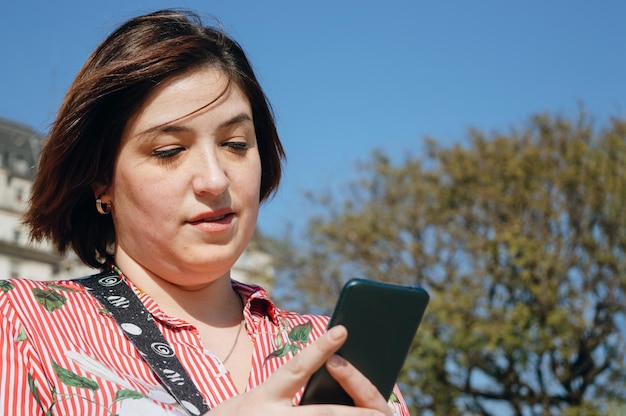 Portret van een jonge latino plus size vrouw die buiten berichten naar haar vrienden aan de telefoon stuurt