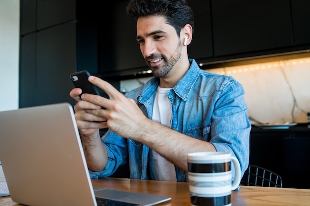 Portret van een jonge man aan het werk met een laptop en zijn mobiele telefoon vanuit huis gebruikt. thuiskantoor concept. nieuwe normale levensstijl.