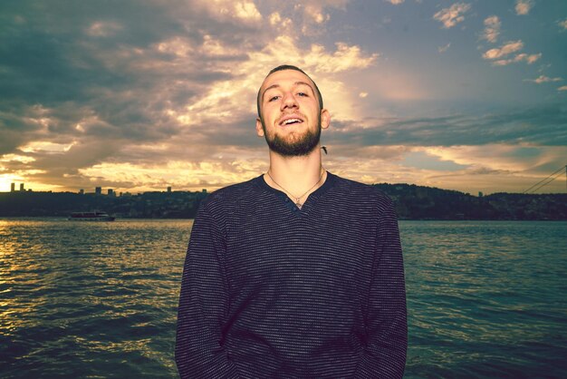 Foto portret van een jonge man die bij zonsondergang tegen de zee staat