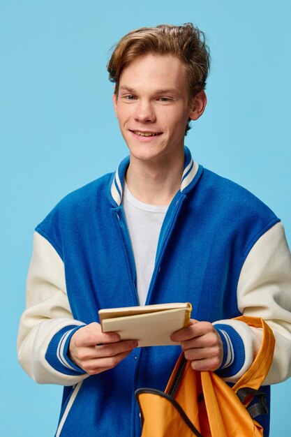 Foto portret van een jonge man die een boek vasthoudt terwijl hij tegen een blauwe achtergrond staat