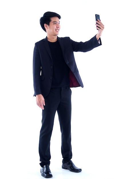 Portret van een jonge man die een selfie met zijn smartphone neemt terwijl hij op wit staat