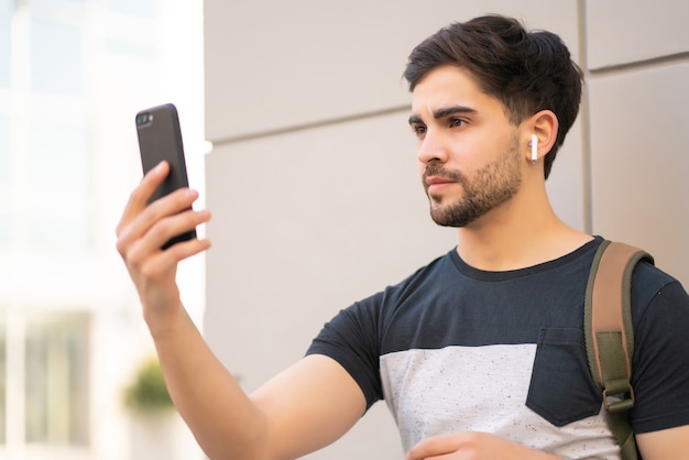 Portret van een jonge man die gezichts-id gebruikt voor het ontgrendelen van de mobiele telefoon terwijl hij buiten staat.