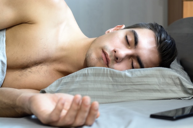 Portret van een jonge man die in bed op een orthopedisch hoofdkussen slaapt, is een speciale vorm voor een gezonde wervelkolom,