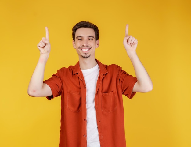 Portret van een jonge man die met de vingers wijst naar kopieerruimte geïsoleerd op gele studioachtergrond