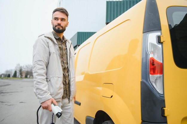 Portret van een jonge man die met oplaadkabel bij het laadstation staat