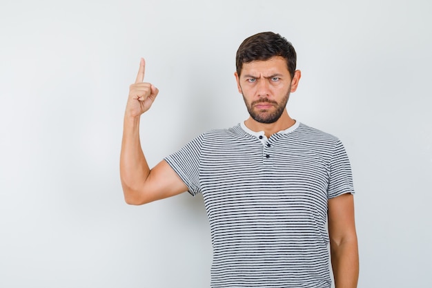 Portret van een jonge man die omhoog wijst in een gestreept t-shirt en er sulky vooraanzicht uitziet