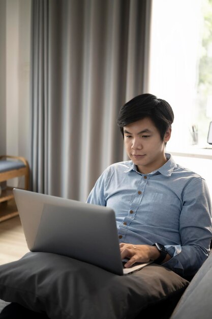 Portret van een jonge man die op een comfortabele bank rust en een laptop gebruikt