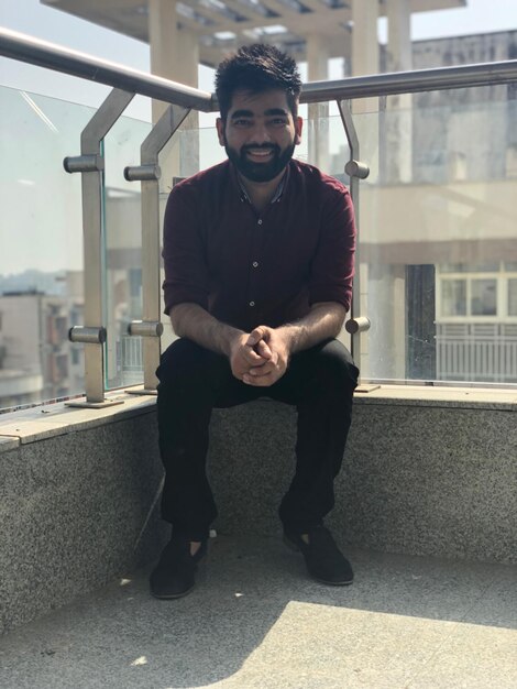 Portret van een jonge man die op een steunmuur zit