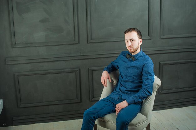 Portret van een jonge man die op een stoel bij de muur zit
