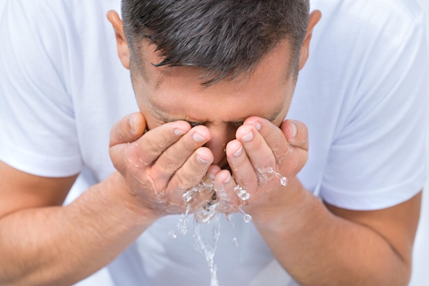 Foto portret van een jonge man die 's ochtends zijn gezicht wast met een scheutje water