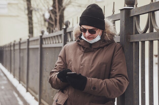 Portret van een jonge man in casual winterkleren met bril en medisch masker op walk city