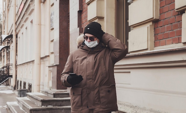 Portret van een jonge man in casual winterkleren met bril en medisch masker
