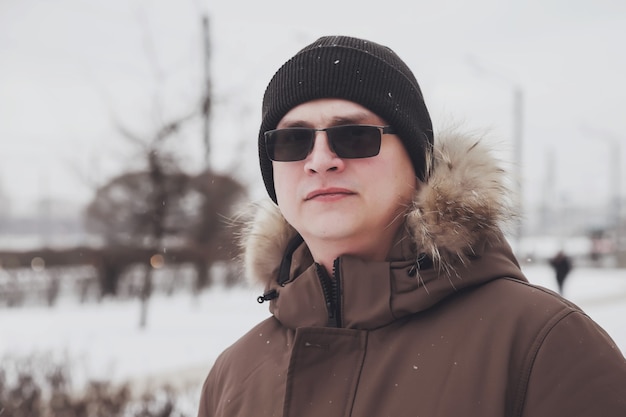 Portret van een jonge man in casual winterkleren met een bril op wandeling stad. Een aantrekkelijke tiener staat in de oude stad en kijkt serieus naar de camera, maar glimlacht lichtjes op een ijzige bewolkte dag. Ruimte kopiëren