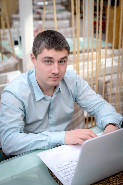 Portret van een jonge man in een blauw shirt op een laptop in een café