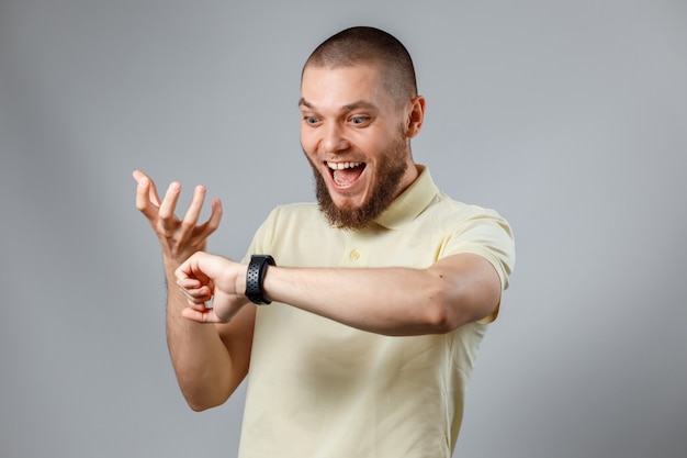 Portret van een jonge man in een geel T-shirt kijkt op zijn horloge op grijs.