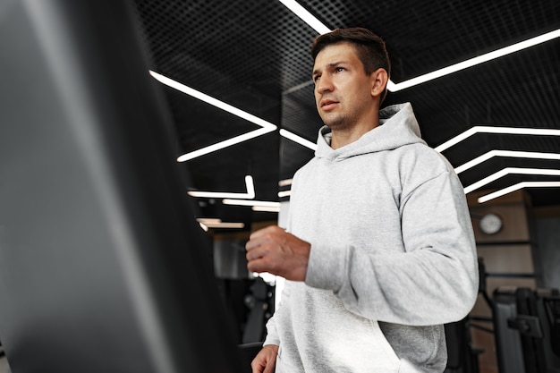 Portret van een jonge man in een oranje windjack die traint op een fitnessapparaat in de sportschool