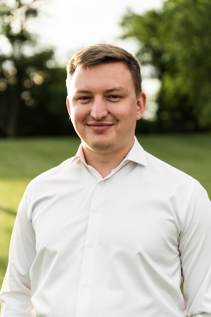 Portret van een jonge man in een wit overhemd wandelen in het park bij zonsondergang. Europese man kijkt naar de camera. man op de achtergrond van het gazon in het park.