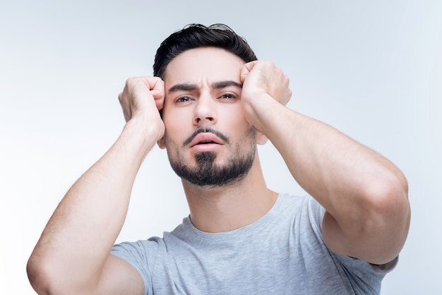 portret van een jonge man in grijs t-shirt poseren tegen een witte muur